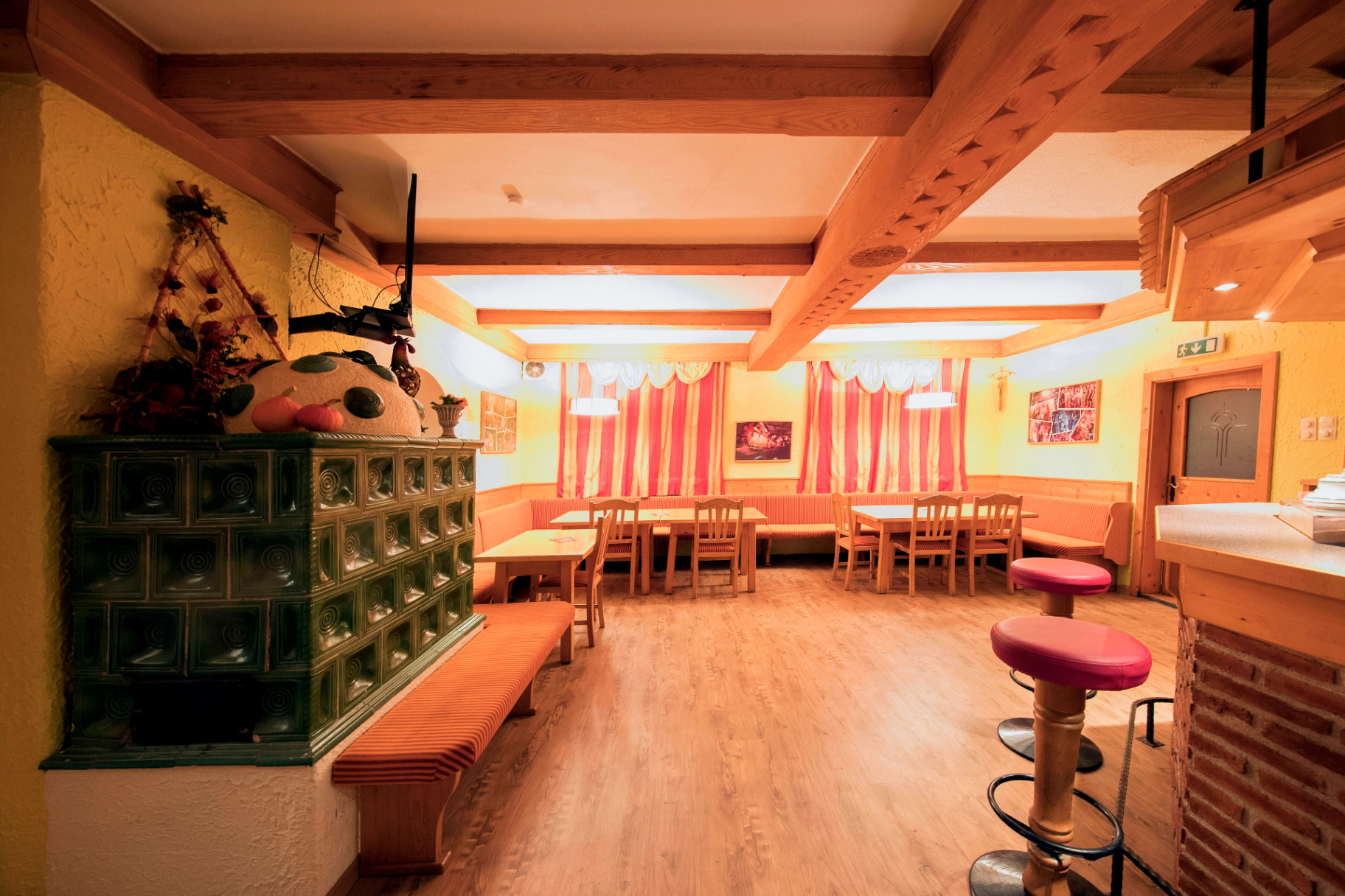 Gemütlicher Gasthaus-Saal mit Holzdecken, Kachelofen, roten Polsterbänken und gedeckten Tischen im warmen Ambiente