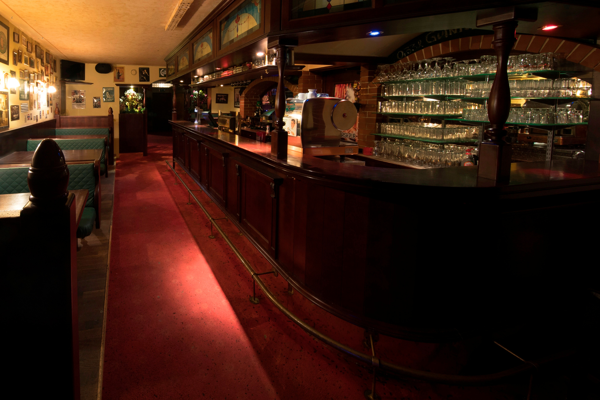 Gemütliche Irish Pub Bar mit dunklem Holztresen, Glasregalen und Sitzbänken im warmen Ambiente